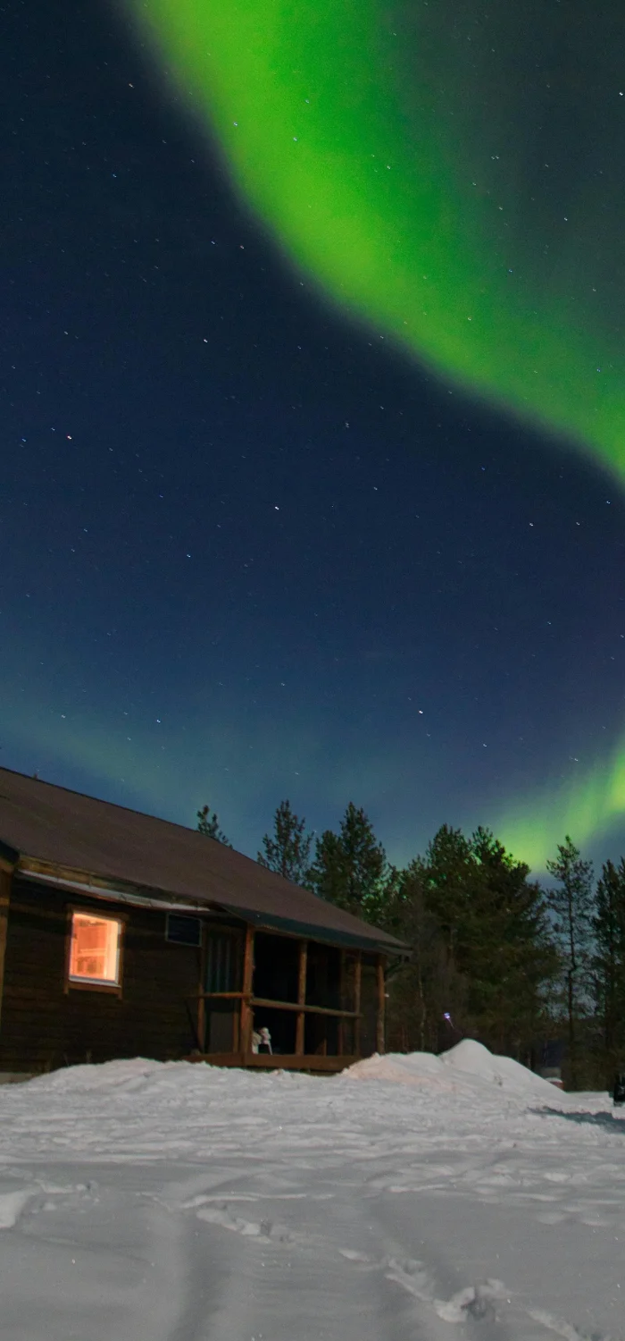 Grönt norrsken ovanför stuga i snötäckt landskap i Kiruna.